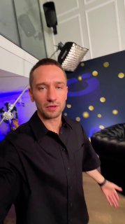 Ведущий в студии UDS DAY на фоне осветительных приборов и декоративной стены с желтыми точками, видна студийная техника.