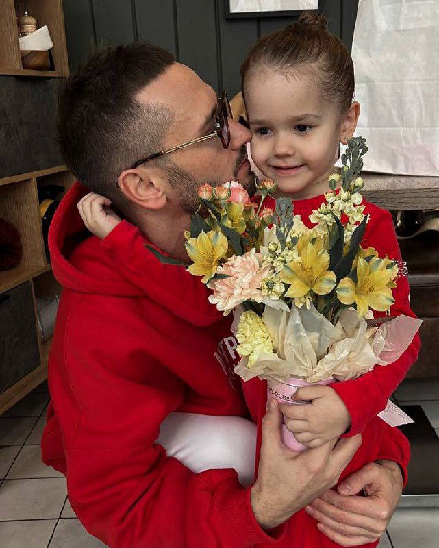 Человек обнимает маленькую девочку с букетом цветов — тёплый семейный кадр, иллюстрирующий отцовскую привязанность и личную мотивацию.