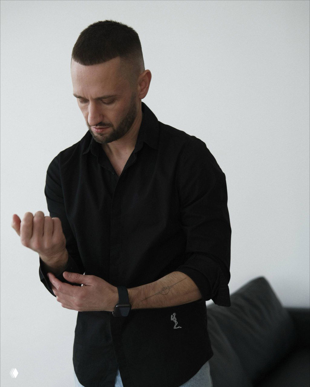 Портретный кадр мужчины в тёмной рубашке в интерьере; спокойная поза и сосредоточенный взгляд создают атмосферу профессионального образа.