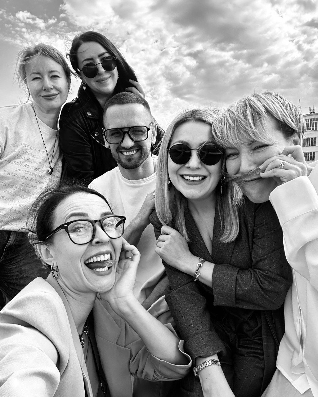 Групповой чёрно‑белый снимок нескольких людей, они улыбаются и обнимаются; атмосферный кадр дружеской команды и коллег.