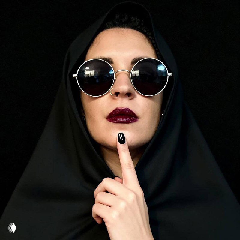 Портрет женщины в тёмном платке и солнцезащитных очках, губы в тёмной помаде, жест пальцем у губ на чёрном фоне — драматичный образ автора