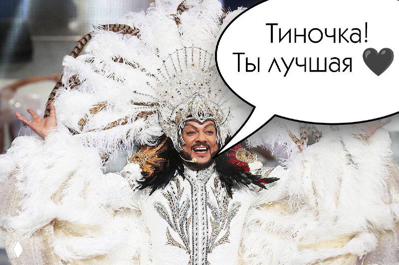 Крупный план исполнителя в пышном белом перьевом костюме и головном уборе; поверх кадра — комиксный пузырь с текстом «Тиночка! Ты лучшая ♥».