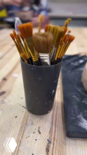 Стакан с кистями на столе гончарной мастерской на размытом фоне — инструменты и рабочая поверхность в кадре.