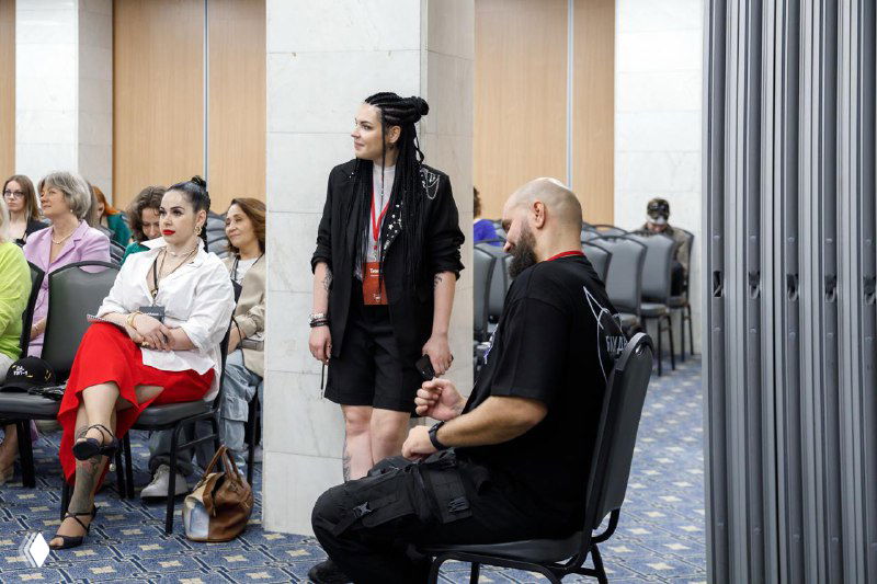 Тина и еще один выступающий в перерыве заседания; наблюдается диалог со зрителями в конференц-зале и активное участие аудитории.