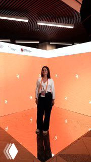 Женщина в деловом образе стоит в яркой оранжевой инсталляции с отражающим полом — атмосферный кадр с мероприятия и портрет участницы.