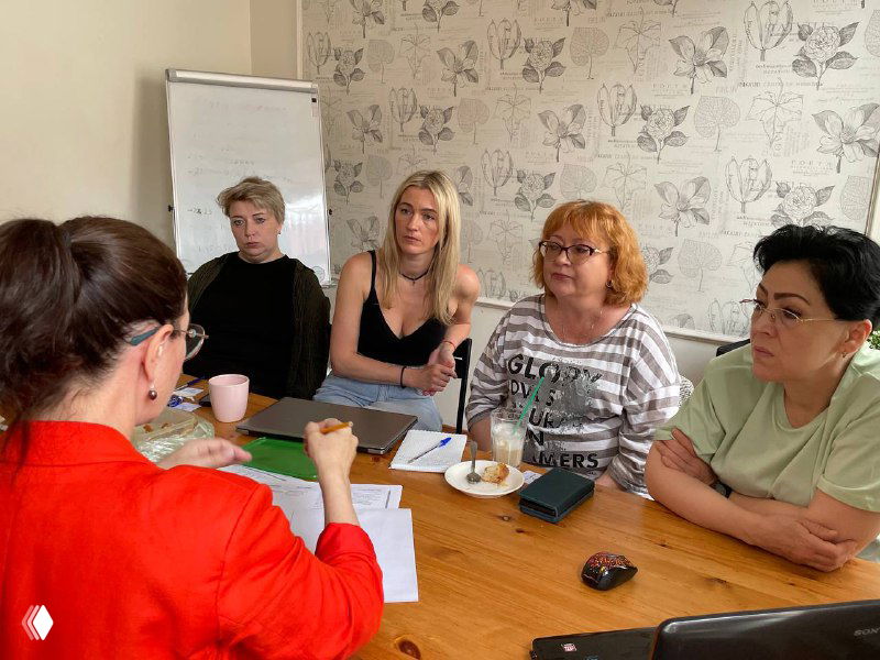 Небольшая группа слушает докладчицу за столом во время встречи по улучшению навыков рекрутеров и менеджеров; обстановка обсуждения кандидатов.