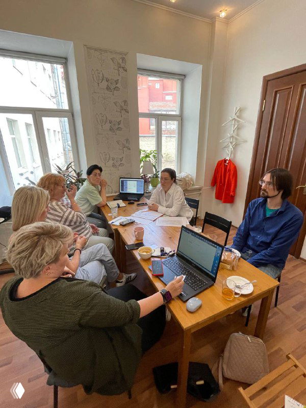 Широкий вид на совещание в офисе агентства: сотрудники сидят за длинным столом с ноутбуками и чашками, внутренняя командная встреча.