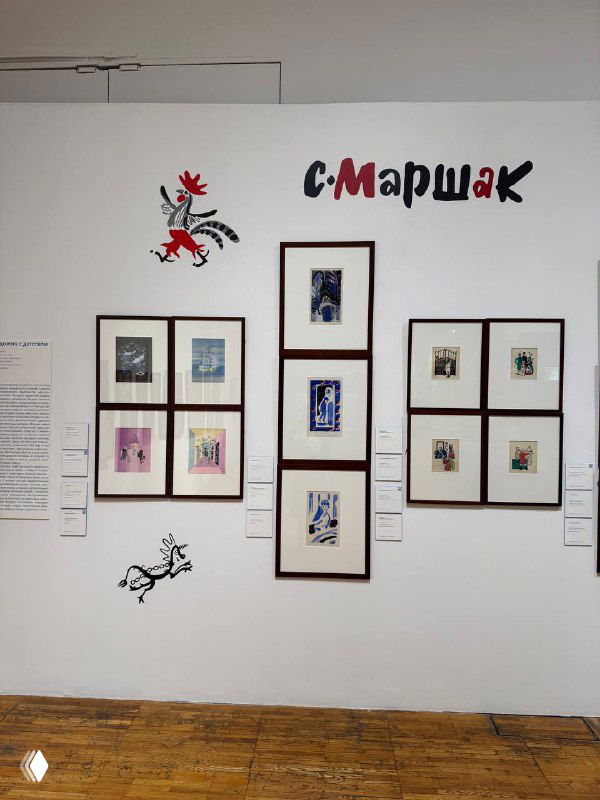 Группа оформленных графических листов и ряд рам на белой стене с надписями и декором в выставочном модуле, общий вид секции экспозиции.