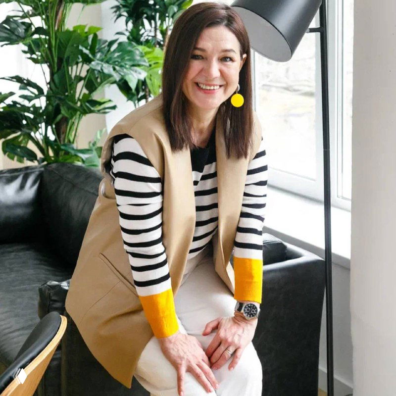 Портрет консультанта по подбору нянь Светланы Тошич: улыбающаяся женщина в жилете в светлом офисе с растениями, профессиональный крупный план.