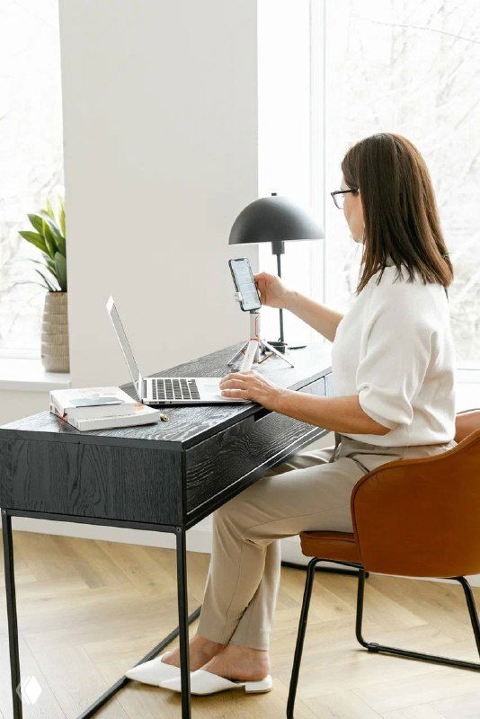 Женщина сидит за рабочим столом с ноутбуком и смартфоном — сценарий выездной встречи HR или консультации по подбору нянь в комфортном месте.