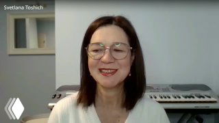 Александра Толкунова улыбается в кадре, в очках, на фоне клавишного инструмента и светлой стены — портрет во время эфира.