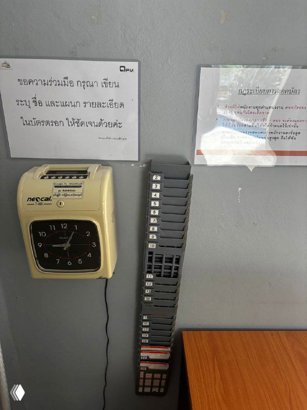 Настенная система учёта рабочего времени: механические табельные часы слева и вертикальная панель с перфорированными карточками для отметок на стене в офисе, интерьер.