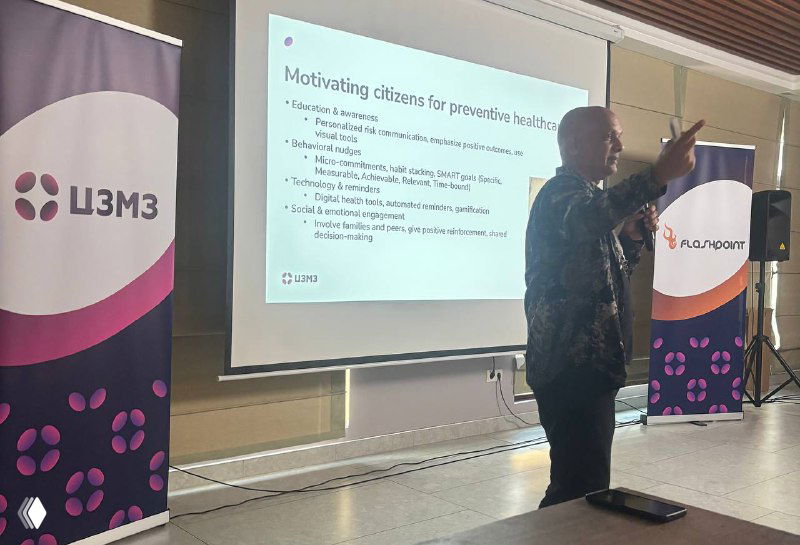 Докладчик на сцене у экрана со слайдами и брендированными баннерами саммита: презентация по превенции и модели управления клиникой в новом рынке