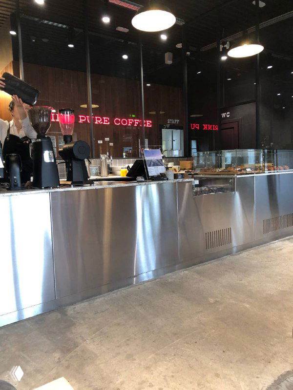 Интерьер современной кофейни: металлическая барная стойка, кофемашина и витрина с выпечкой, вид с прохода у входа.