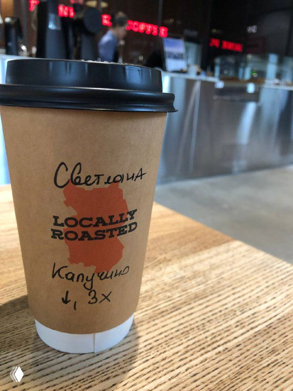 Бумажный стакан с крышкой на столе: имя «Светлана», штамп 'Locally Roasted' и пометка 'капучино' — пример персонализации заказа.