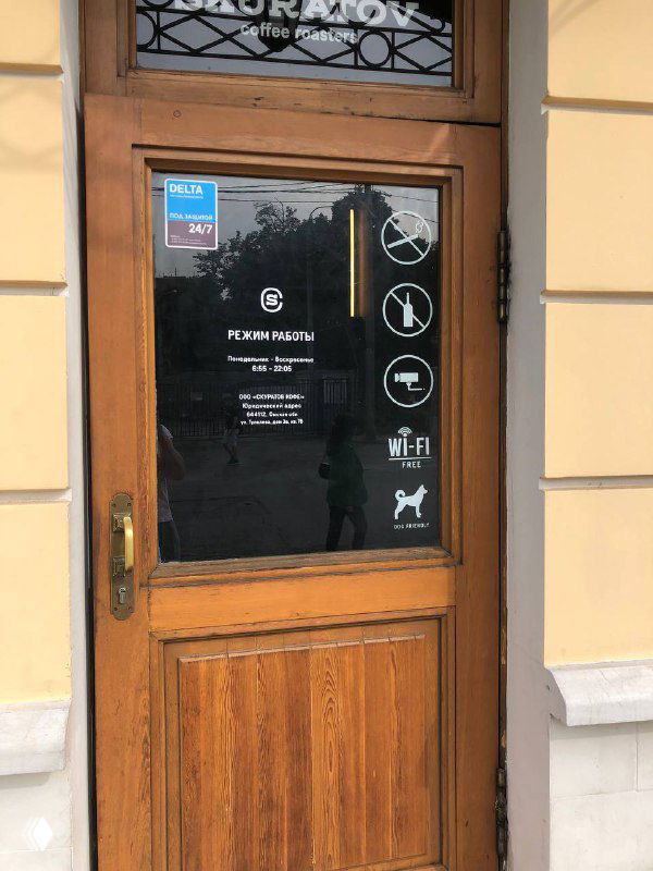 Деревянная входная дверь кофейни с наклейками и пиктограммами (Wi‑Fi, питомцы, запреты) и частью фасада здания.