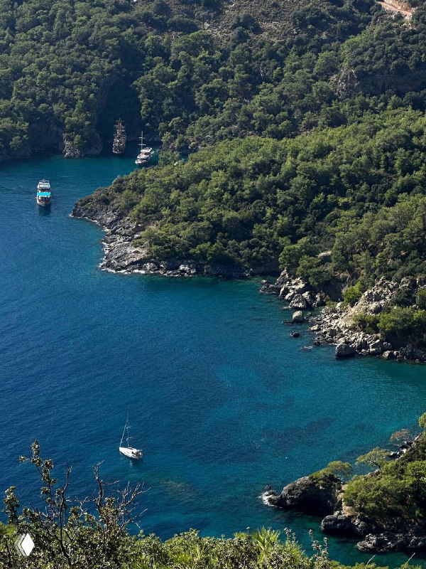 Бухта с яхтами и каменистым берегом, глубокий сине-зеленый цвет воды и заросли кипарисов на склонах — тихая морская бухта на тропе.