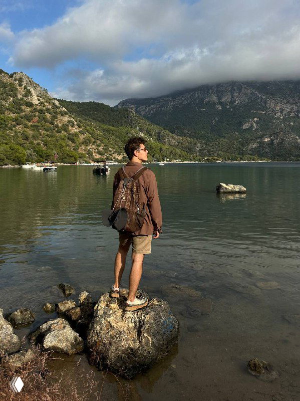 Пейзаж с человеком на камне и тучами над горным хребтом, сочетание спокойной воды и драматичного неба — вечерние мотивы маршрута.