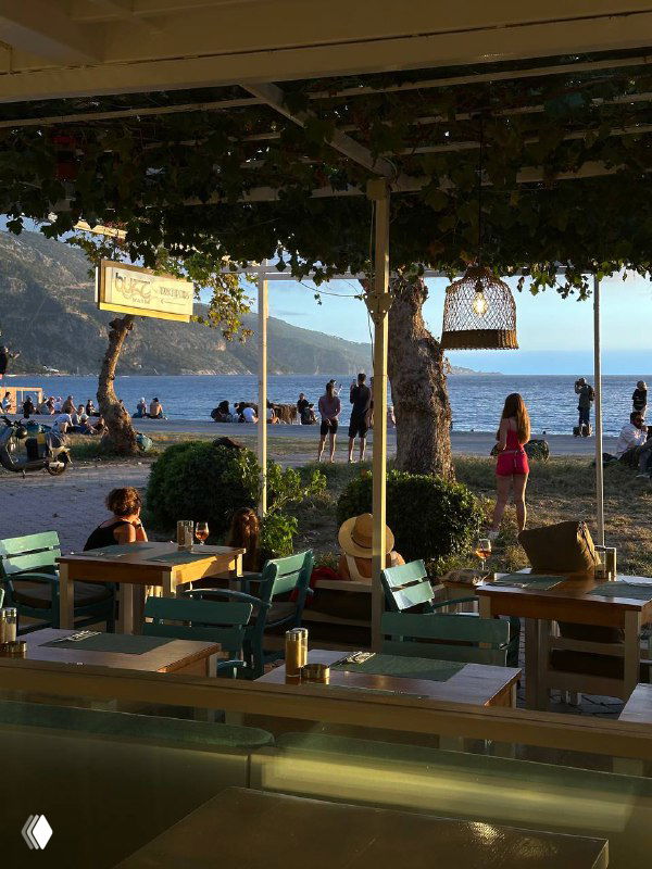 Набережная Олюдениза в закатном свете: столики кафе, люди у пляжа, золотой свет и спокойная вечерняя атмосфера после дня в походе.