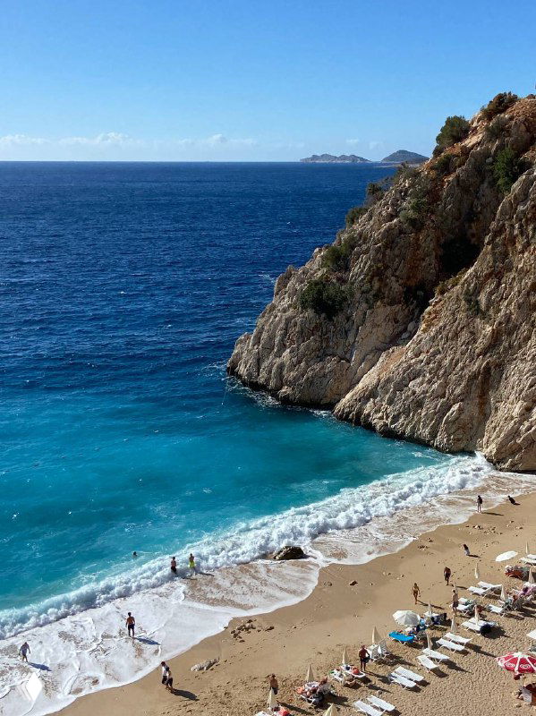 Панорамный вид на пляж с бирюзовой водой, лежаками и отдыхающими у побережья между Каша и Калканом при ясной погоде и спокойном море.