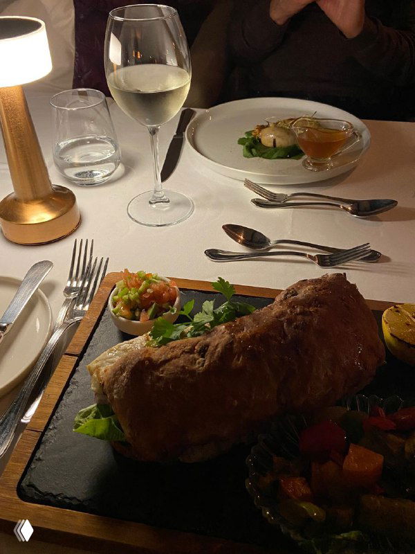 Блюдо на белой скатерти, бокал белого вина и аккуратно сервированный стол — пример подачи в панорамном ресторане Mikla.