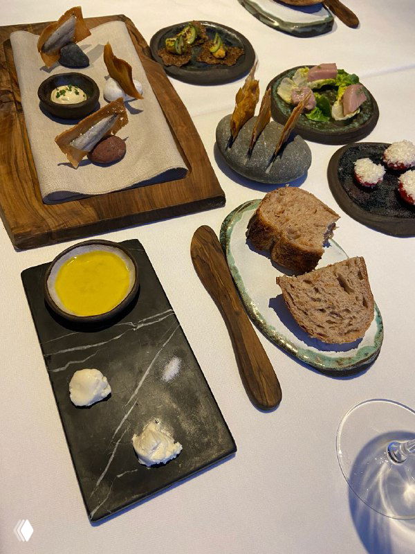 Набор закусок и хлеба на деревянной доске, мелкие порции и элементы авторской подачи в ресторане высокой кухни.