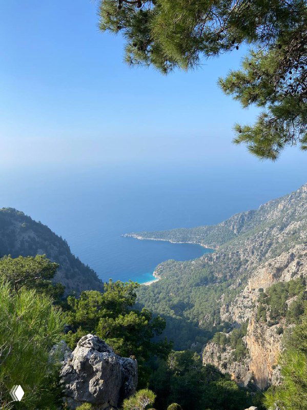 Панорамный вид с горной дороги на хвойные склоны и бирюзовое море вдалеке; изгибы трассы и прибрежный пейзаж турецкого побережья.