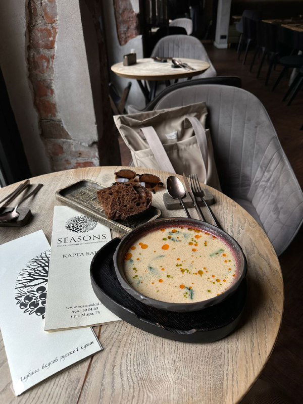 Тарелка балтийской сливочной ухи на деревянном столе в уютном кафе Калининграда: суп, хлеб и меню рядом, кадр подчёркивает гастрономическую сцену города.