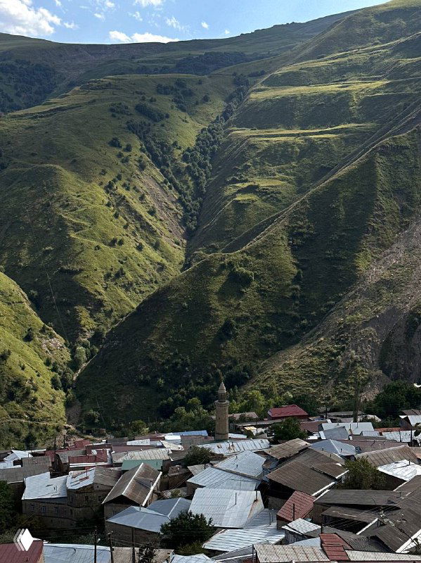 Панорамный вид на горную долину и крыши аульских домов в Дагестане, террасы и крутые склоны под ясным небом.