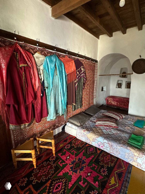 Спальная комната в сакле с развешанными национальными платьями, коврами и деревянной мебелью, уютный аутентичный интерьер.