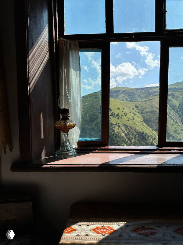 Окно комнаты с видом на горы: свет через стекло, долина внизу и рисунок неба над дагестанскими склонами.