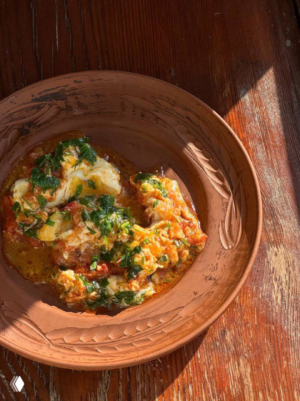 Блюдо аварского чуду в керамической тарелке на деревянном столе, видна зелень, соус и традиционная подача домашней выпечки.