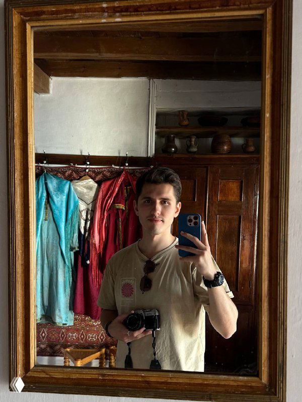 Зеркальное селфи туриста в интерьере сакли с отражением деревянной мебели, традиционных текстильных элементов и посуды.