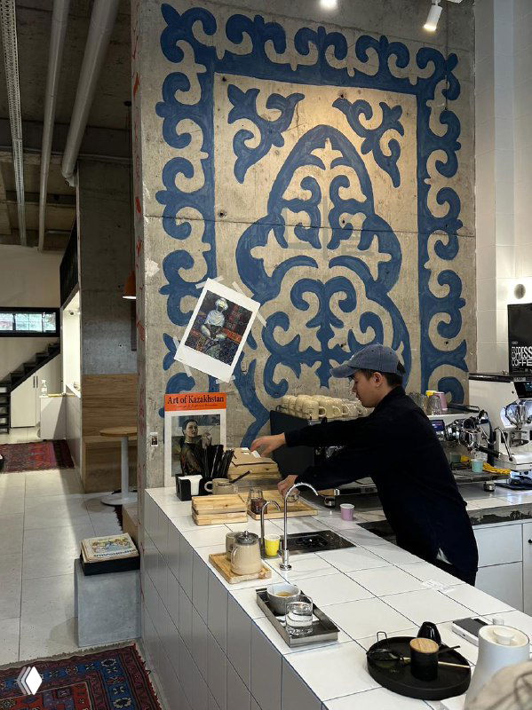 Современное кафе-арт-пространство с крупным киргизским орнаментом на стене и бариста за стойкой — сочетание традиций и креативной городской среды.