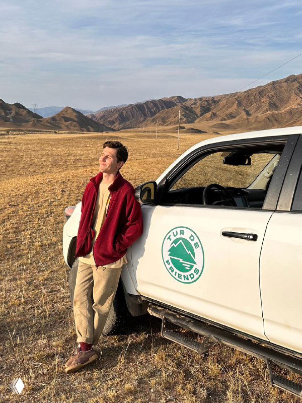 Путешественник у внедорожника с логотипом Tur de Friends на фоне открытой равнины и гор — часть экспедиции и логистика поездки.
