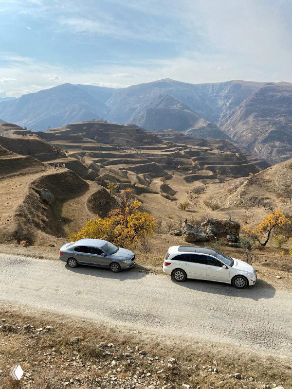 Дорога в горной местности Дагестана: две машины на просёлочной трассе, окружающая осенняя растительность и террасы на склонах.