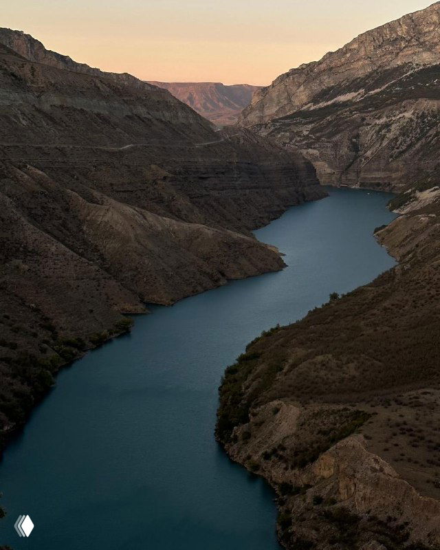 Узкое водохранилище между высокими скалами в Дагестане на закате: сдержанные тёплые тона и спокойная поверхность воды.