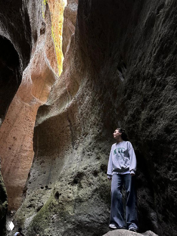 Узкий каньон внутри скал, где турист позирует в мягком свете; ощущение тесных вертикальных стен и текстуры породы.