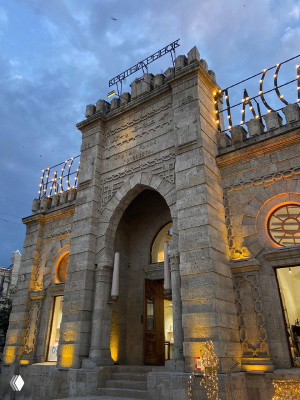 Нарядный фасад здания вокзала или исторической станции в вечерней подсветке на фоне тёмнеющего неба в одном из дагестанских городов.