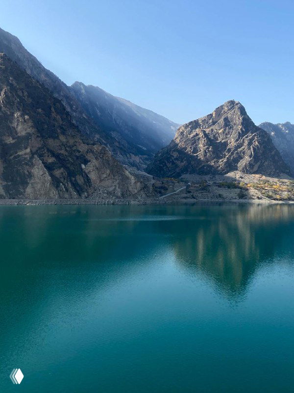 Бирюзовое горное озеро в ясную осеннюю погоду, окружённое крутыми скалами и чистым небом, отражающимся в воде.