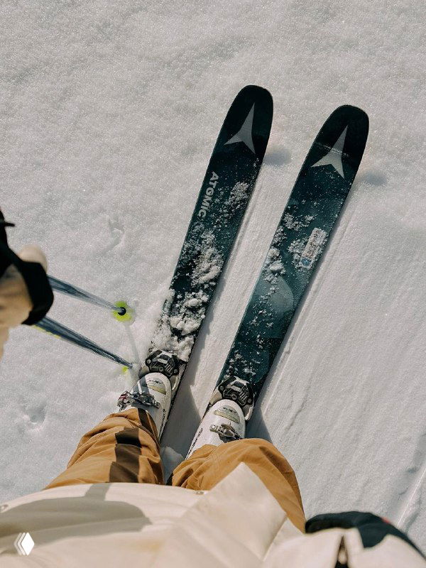 Вид вниз на лыжи и ботинки лыжника, подготовленный склон с мягким снегом и следами — кадр непосредственно во время катания на курорте.