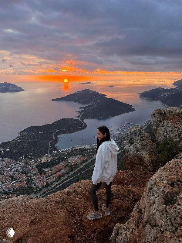 Вид со смотровой площадки на бухту и острова при ярком восходе/закате; человек на переднем плане добавляет масштаба пейзажу.