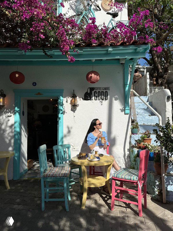 Яркое кафе в старом квартале с цветущими растениями и столиком на улице, в кадре человек, наслаждающийся напитком в тёплом свете.