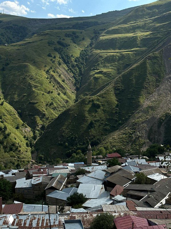 Панорама горного ущелья и крыши аульских домов на фоне зелёных склонов — пейзаж Дагестана и уклад жизни в горах.