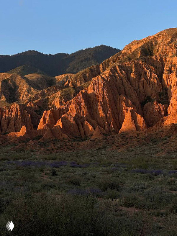 Огненно‑красные скальные формации и зубчатые гребни в кыргызском каньоне, драматичный пейзаж с выраженной текстурой и игрой света.