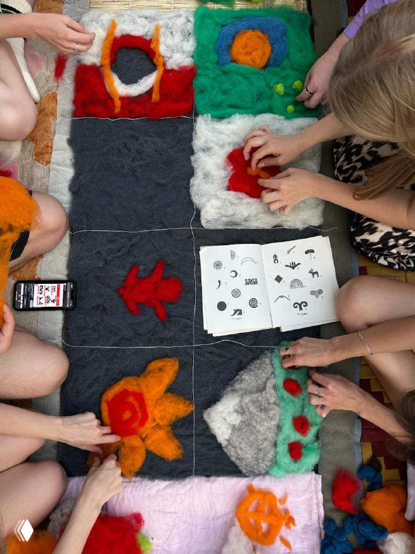 Мастер-класс по сухому валянию: несколько людей раскладывают цветную шерсть и формируют орнамент будущего шерстяного ковра «ширдак».