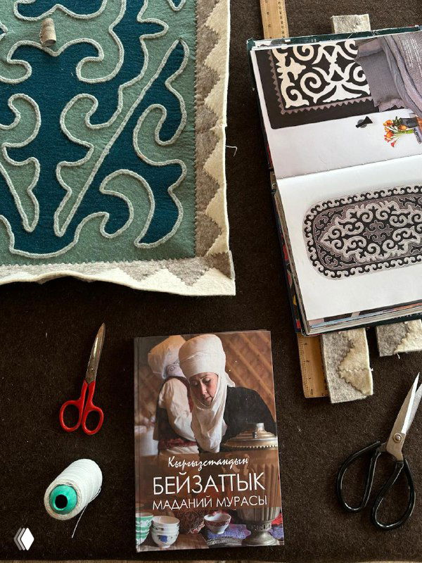 Рабочее место: куски текстиля, книги по орнаментам и инструменты для обработки шерсти и изготовления ковров и ремесленных изделий.