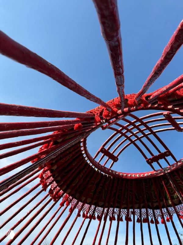 Вид снизу на центральную часть юрты: деревянные лучи и красная тканевая обивка, конструкция крыши и характерная форма купола.