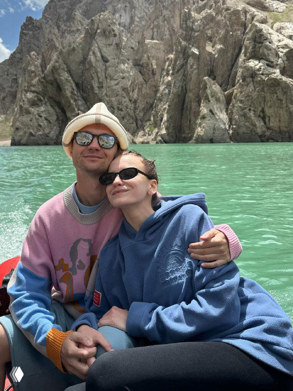 Пара на лодке в бирюзовом горном озере: улыбки, солнцезащитные очки и спокойная водная гладь на фоне скалистых берегов.