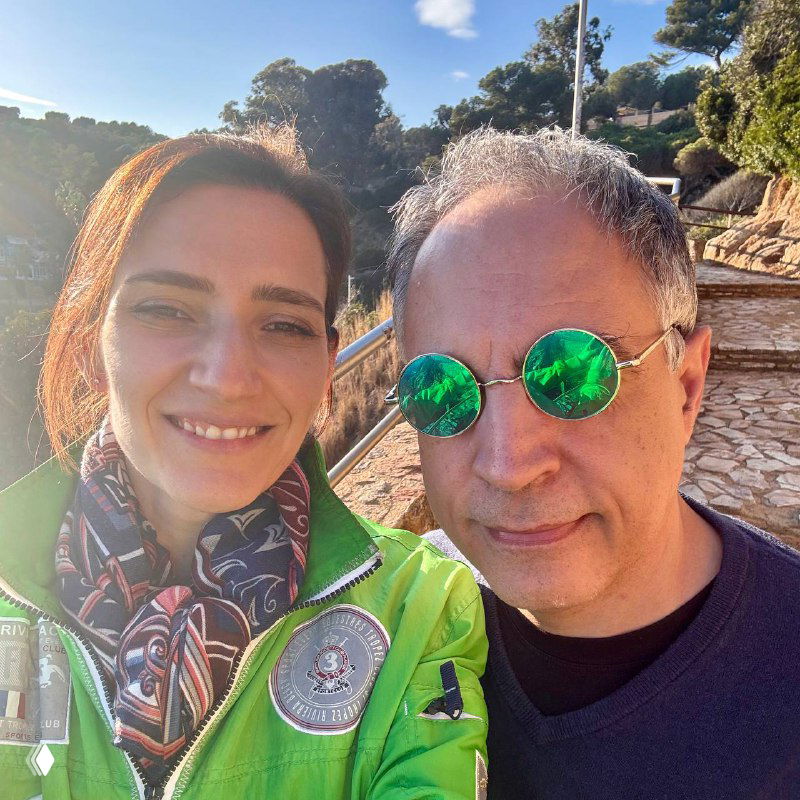 Селфи женщины и мужчины на солнечной набережной: оба улыбаются, мужчина в ярких зелёных очках, тёплая дружеская атмосфера.